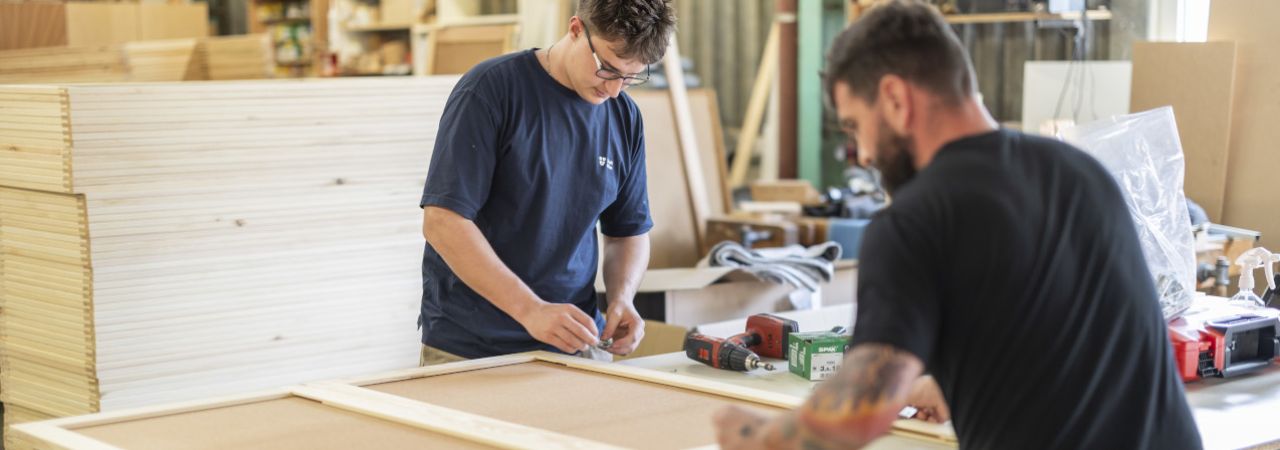 Zwei Männer schrauben Holzpaneele zusammen.