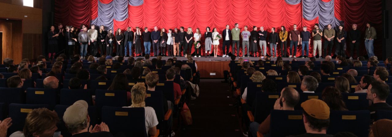 Gefüllter Kinosaal mit Künstler*innen auf der Bühne im Gartenbaukino