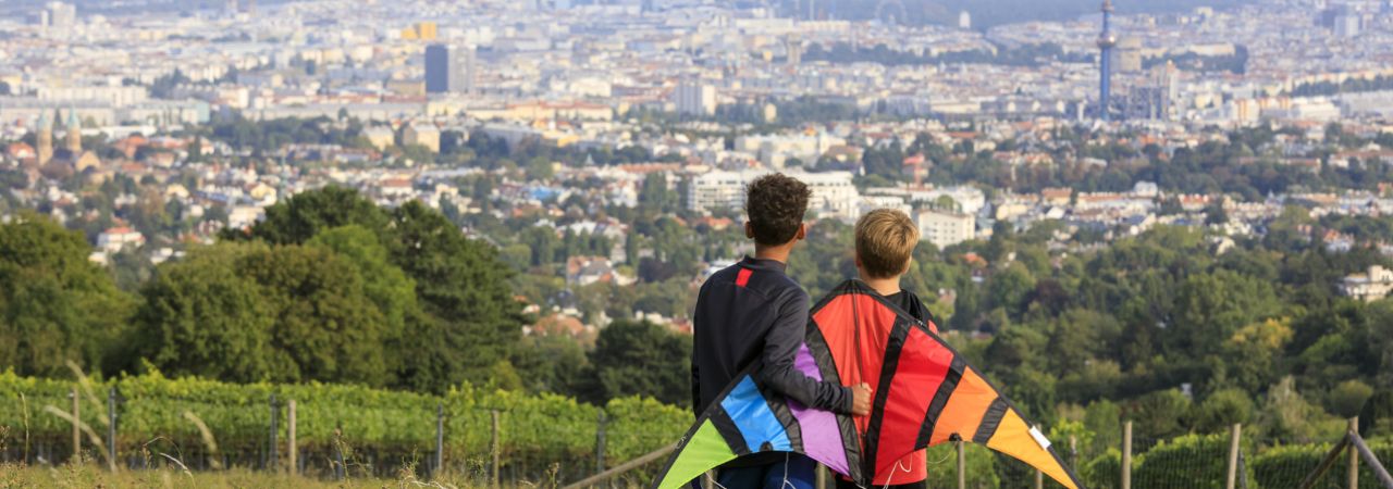 Zwei Kinder mit Papierdrachen genießen die Aussicht auf die Stadt Wien