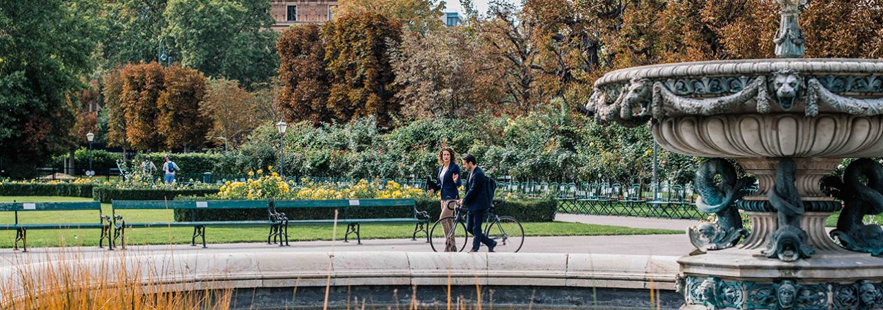 Spaziergänger*innen schlendern bei Brunnen vorbei